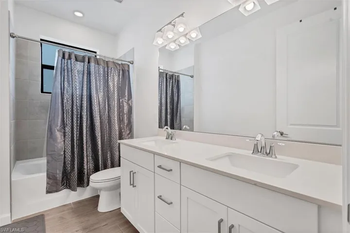 Full bathroom with shower / bath combo, double vanity, light wood-style floors, and recessed lighting