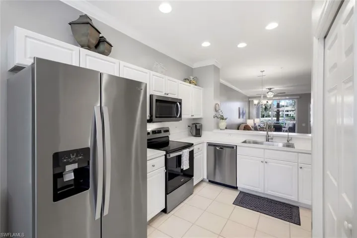 Kitchen with sink, light tile patterned floors, ornamental molding, white cabinetry, and stainless steel appliances