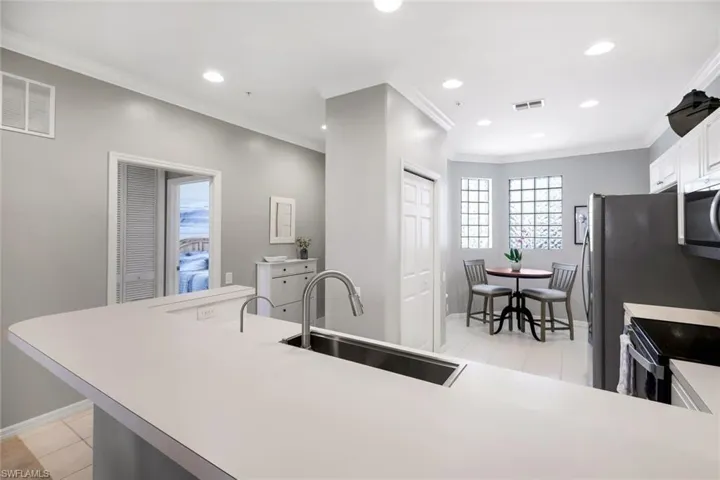 Kitchen with sink, light tile patterned floors, appliances with stainless steel finishes, white cabinets, and ornamental molding
