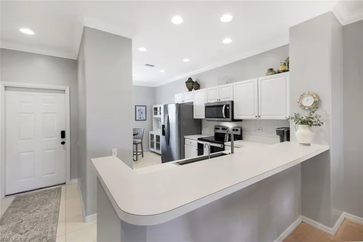 Kitchen with backsplash, kitchen peninsula, a breakfast bar area, white cabinets, and appliances with stainless steel finishes