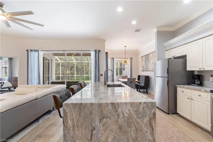 Kitchen featuring sink, crown molding, pendant lighting, light hardwood / wood-style floors, and a center island with sink
