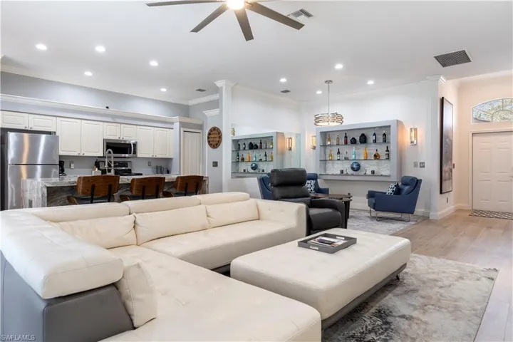 Living room with bar area, ceiling fan, ornamental molding, and light hardwood / wood-style flooring