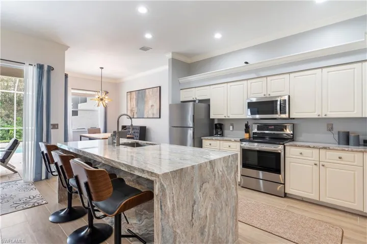 Kitchen featuring light stone countertops, appliances with stainless steel finishes, a kitchen island with sink, and sink