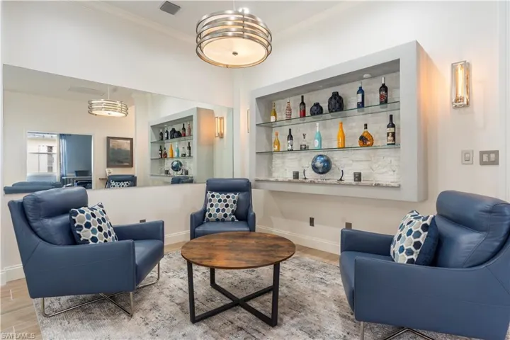 Living room with bar area, built in shelves, ornamental molding, and light wood-type flooring