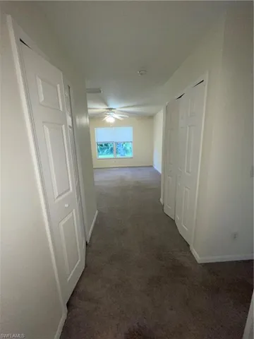 Hallway featuring dark colored carpet and baseboards