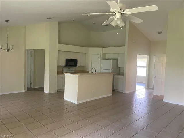 Kitchen featuring high vaulted ceiling, black microwave, a center island with sink, a ceiling fan, and light tile patterned floors