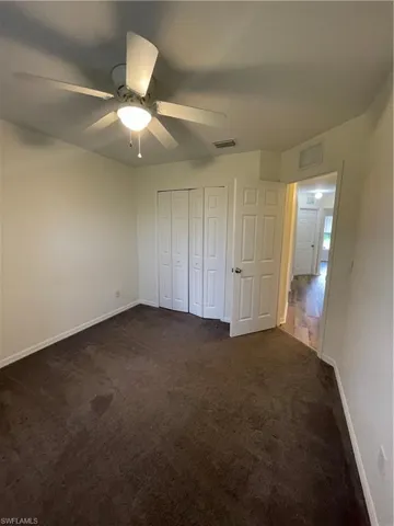 Unfurnished bedroom with dark carpet, a ceiling fan, and a closet