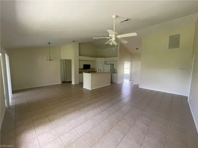 Unfurnished living room with light tile patterned floors, ceiling fan, high vaulted ceiling, and a chandelier