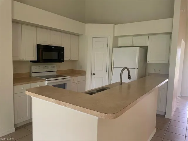 Kitchen featuring light tile patterned floors, white appliances, white cabinetry, light countertops, and a center island with sink