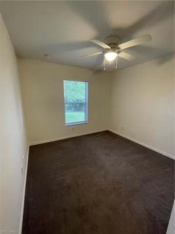 Empty room featuring dark carpet and baseboards