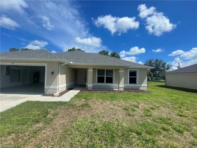 Rear view of property featuring a garage, a lawn, a shingled roof, stucco siding, and driveway