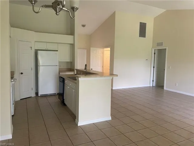 Kitchen with white appliances, high vaulted ceiling, light tile patterned floors, white cabinets, and open floor plan