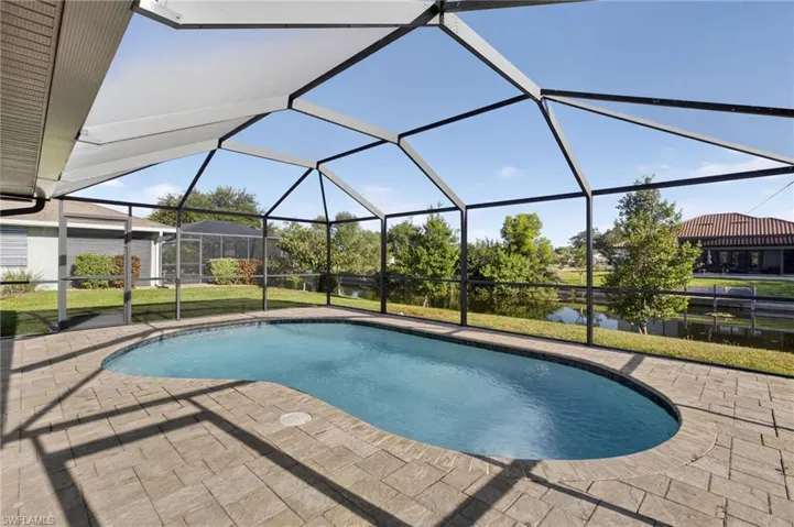 Swimming pool featuring a patio area, glass enclosure, a lawn, and a water view