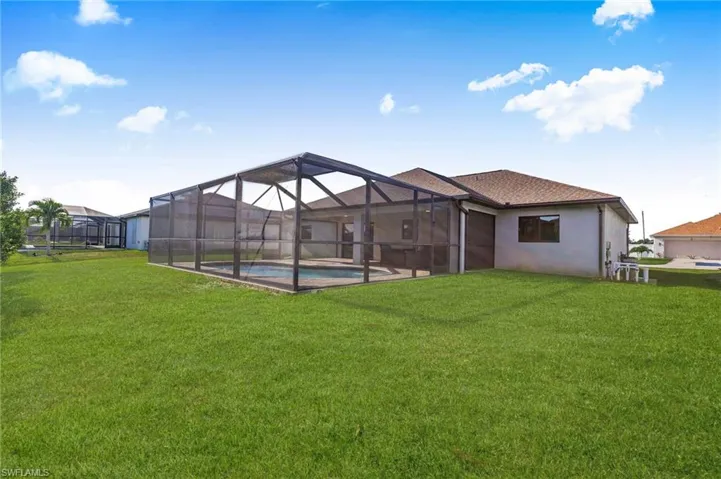Back of house with a lawn, stucco siding, an outdoor pool, and glass enclosure