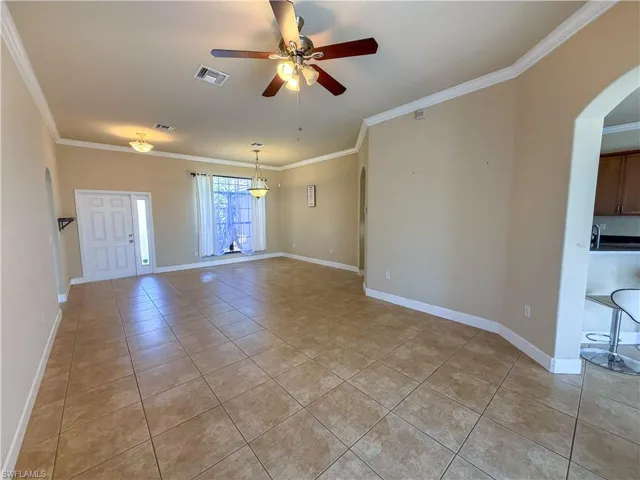 Empty room with arched walkways, ornamental molding, a ceiling fan, and light tile patterned floors