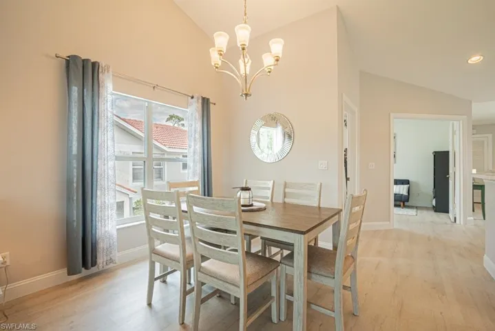 Dining space with light wood-style floors, a notable chandelier, and vaulted ceiling