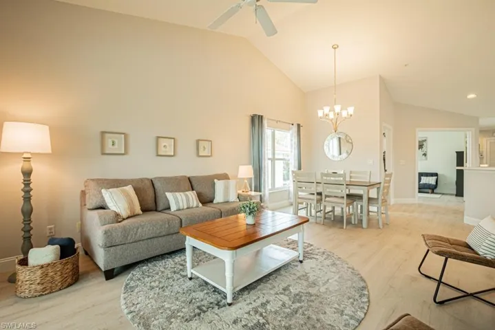 Living room with light hardwood / wood-style floors, high vaulted ceiling, and ceiling fan with notable chandelier