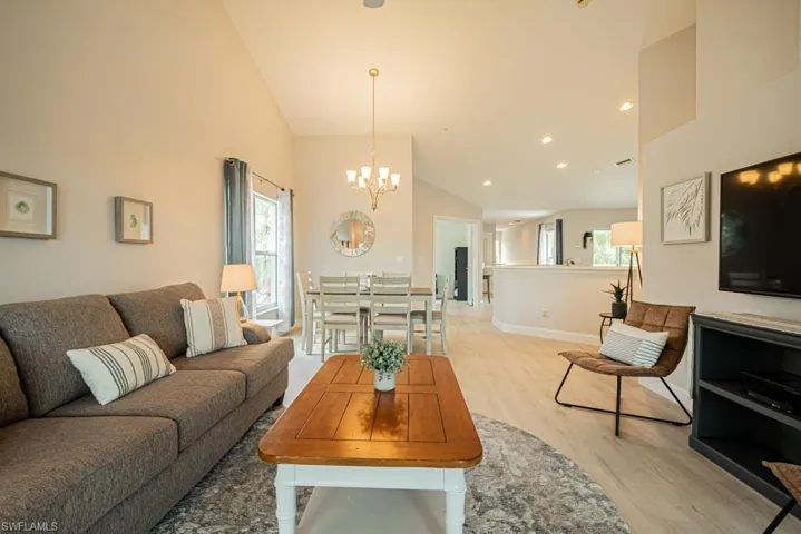 Living room with a notable chandelier, high vaulted ceiling, and light wood-type flooring