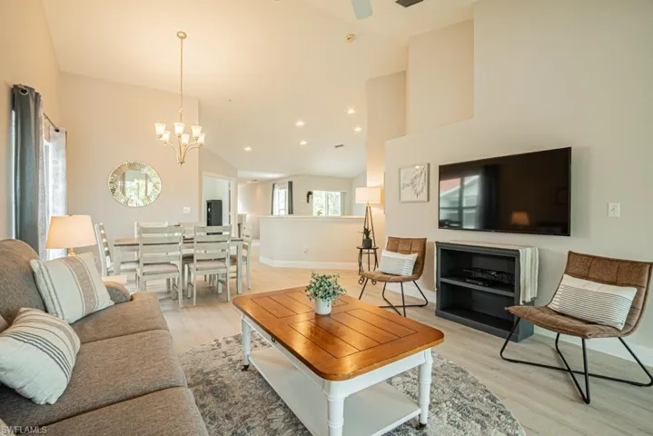 Living room with light wood-style flooring, high vaulted ceiling, and ceiling fan with notable chandelier