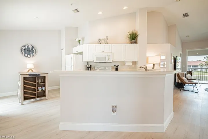 Kitchen featuring white appliances, sink, light wood-type flooring, white cabinetry, and high vaulted ceiling
