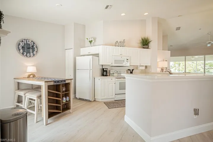 Kitchen featuring light wood-style floors, lofted ceiling, white cabinetry, and white appliances