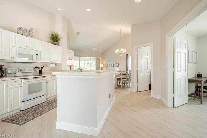Kitchen with lofted ceiling, light wood-type flooring, a chandelier, white cabinetry, and white appliances