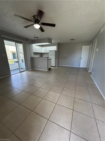 Unfurnished living room with a textured ceiling, light tile patterned floors, and a ceiling fan