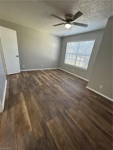 Unfurnished room featuring a textured ceiling, a ceiling fan, and dark wood-style flooring