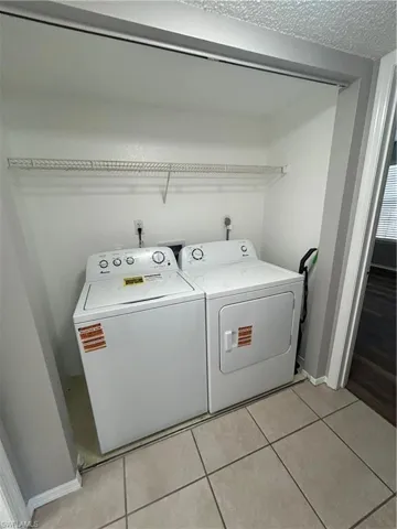 Laundry area with washing machine and clothes dryer, light tile patterned floors, and a textured ceiling