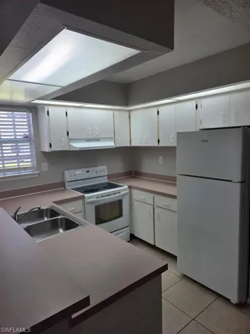 Kitchen featuring white appliances, white cabinetry, light tile patterned floors, and light countertops