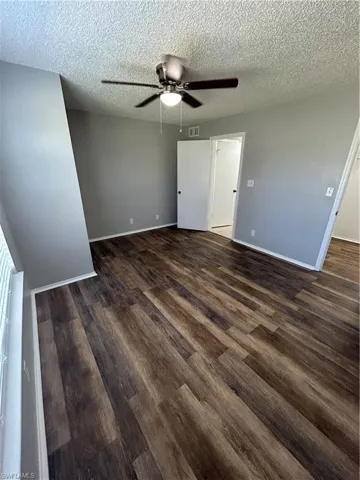 Unfurnished bedroom featuring dark wood-style flooring, a textured ceiling, and a ceiling fan