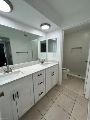 Full bathroom featuring double vanity, light tile patterned flooring, and a shower stall