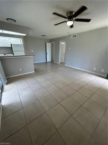 Unfurnished living room featuring light tile patterned floors, a ceiling fan, and a textured ceiling
