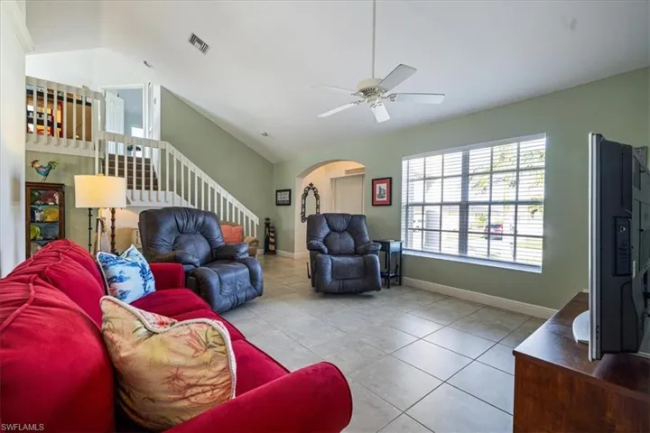 Living room featuring vaulted ceiling, ceiling fan, and light tile patterned flooring