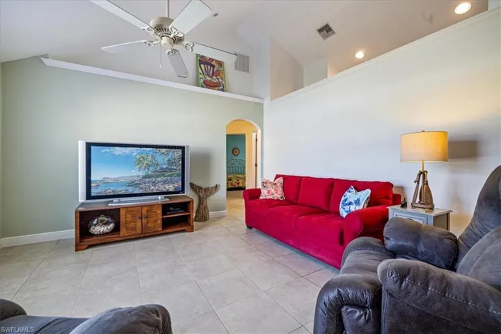 Tiled living room featuring high vaulted ceiling, ceiling fan, and crown molding