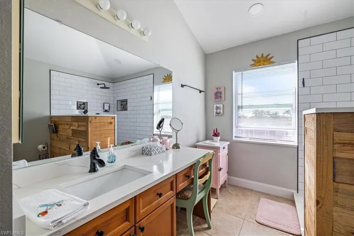 Bathroom featuring a tile shower, tile patterned flooring, vanity, and vaulted ceiling
