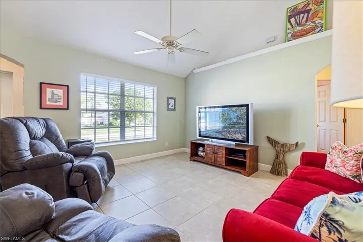 Tiled living room featuring ceiling fan, lofted ceiling, and crown molding