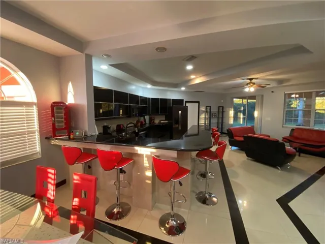 Kitchen with ceiling fan, sink, kitchen peninsula, a tray ceiling, and light tile patterned floors
