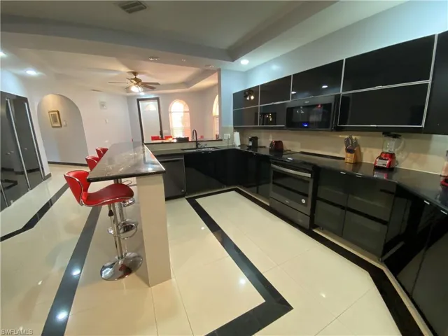 Kitchen with black appliances, a raised ceiling, sink, ceiling fan, and light tile patterned floors