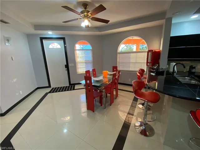 Tiled dining space featuring ceiling fan, sink, and a tray ceiling