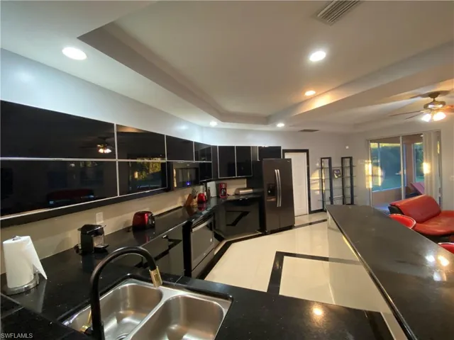 Kitchen featuring sink, light tile patterned floors, stainless steel refrigerator with ice dispenser, and a tray ceiling