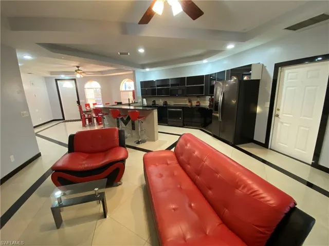 Living room with ceiling fan, light tile patterned flooring, and a tray ceiling