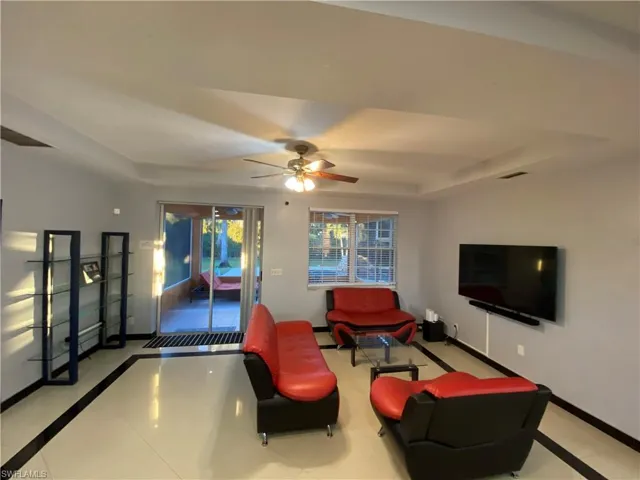Living room with ceiling fan, light tile patterned flooring, and a tray ceiling