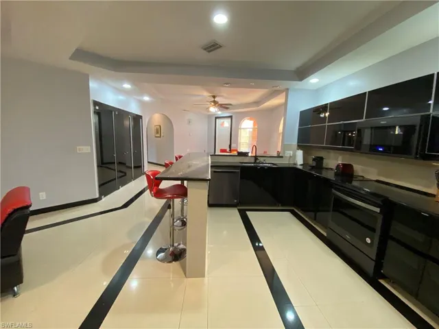 Kitchen with stainless steel dishwasher, light tile patterned flooring, a raised ceiling, and sink