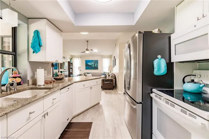 Kitchen featuring a tray ceiling, white appliances, ceiling fan, and white cabinetry