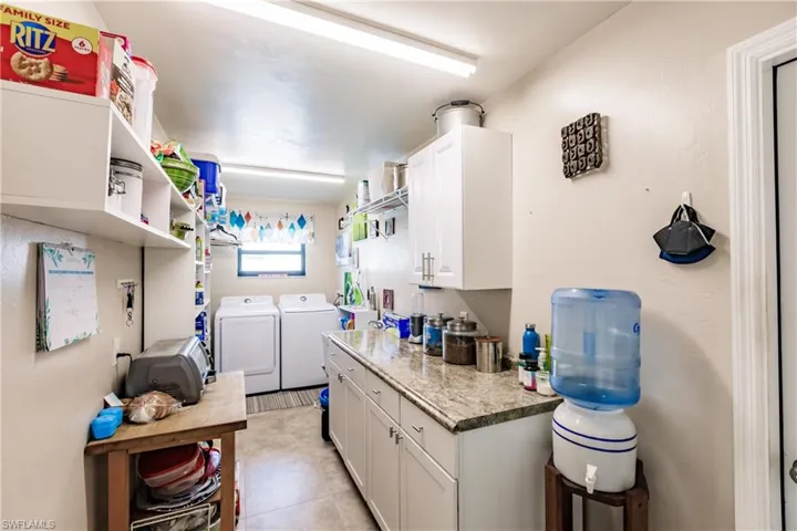 Kitchen with washer and dryer, light tile patterned flooring, light stone countertops, and white cabinets