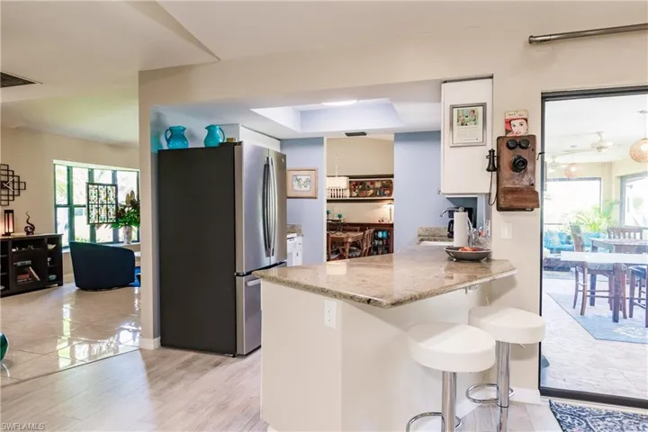 Kitchen with a raised ceiling, light wood-type flooring, kitchen peninsula, stainless steel fridge, and a breakfast bar