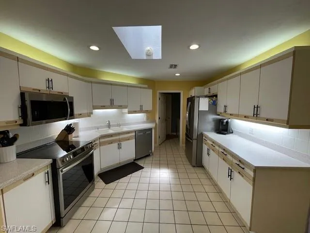 Kitchen with appliances with stainless steel finishes, white cabinetry, decorative backsplash, and sink