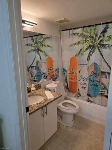Bathroom featuring vanity, shower / bathtub combination with curtain, light tile patterned floors, and a textured ceiling