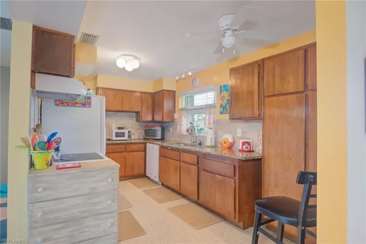 Kitchen with brown cabinets, backsplash, under cabinet range hood, and white appliances
